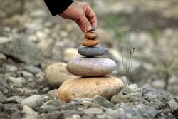 Zen-style stone pyramid in a natural setting with a hand that gently places a stone on top, which conveys peace, harmony and respect for nature