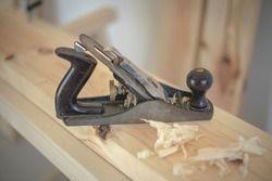 Close-up of old and traditional black metallic wood planer on wooden plank in a carpentry shop with natural light