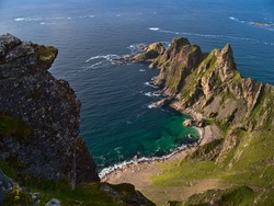 Aerial view of the rough coast of the Norwegian Sea in the north of Andøya island, Vesterålen, Norway with beautiful turquoise colored rock beach, mountains and rugged cliffs on sunny summer day.
