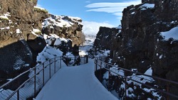 Diminishing perspective of snow-covered hiking path leading through Almannagjá gorge in Þingvellir national park, Iceland, a rift valley of Mid-Atlantic Ridge with steep cliffs on sunny winter day.