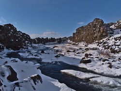 Beautiful view of small stream near Öxarárfoss in Þingvellir national park, Golden Circle, Iceland, flowing through a tectonic rock gap with snow and ice on sunny winter day.