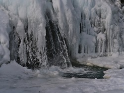Close-up view of frozen cascade Kirkjufellsfoss near Grundarfjörður on Snæfellsnes peninsula, west Iceland in winter season with splashing water, snow, ice formations and icicles.