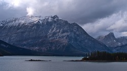 Beautiful panoramic view over reservoir Upper Kananaskis Lake in Alberta, Canada in the Rocky Mountains with forest on the rocky shore and the snow-capped peak of rugged Mount Lyautey in autumn.