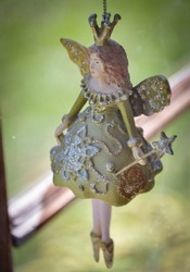 a doll of a fairy hanging in front of a window, she has a green dress and a crown, also a scepter in the shape of a star.
