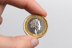 Hand holding a coin of one pound sterling with the image of Queen Elizabeth II close-up on a white background. UK currency.