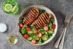 Grilled healthy chicken breast with a salad of cherry tomatoes, cucumbers, arugula and parsley.