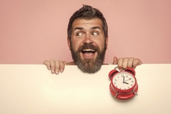 Time management and business success. Guy with happy face hold white paper. Hipster with red clock on pink background. End of working day or perfect morning. Man with long beard hold alarm clock.