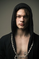 Brutal young man wearing hooded black outfit and bicycle around his neck isolated on gray background, troublemaker and hooligan, growing up at streets.