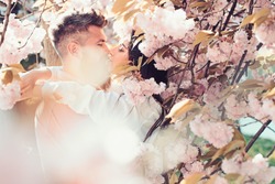 Man and woman kissing in blooming garden on spring day. Couple hugs near sakura trees. Couple in love spend time in spring garden, flowers on background, defocused, close up. Passion and love concept.