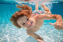 Happy kid boy swim and dive underwater, kid with fun in pool under water. Active healthy lifestyle, water sport activity and swimming lessons on summer vacation with child.
