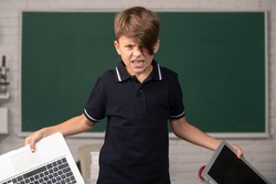 Angry boy in opposition distance education. School kid broken online laptop. Smashing damaged cracked computer technology. Kids problem with remote learning in class.