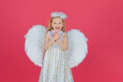 Excited child girl with angel wings, studio portrait. Valentine gift card. Cute angel child girl with angels wings, isolated on red. Valentines day.