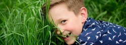 Banner with spring child face. Smiling child boy with grass background. Cute kid enjoying on field. Unity with nature. Kids on green grass background.