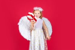 Angel children girl with white wings Cute baby child with angel wings. Angel kids with present gift, studio portrait. Little blonde angel with white wings holds gift. Valentine gift card.