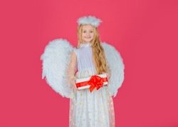 Child angel little girl with present gift, studio portrait. Girl prince greeting card. Little angel with white wings holds gift. Playful angelic little girl. Valentines day.