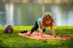 Child is pushing up on the green meadow, working out wearing sportswear, t-shirt outdoor. Kids doing push up outdoor. Gymnastic for children. Kid pushing up.