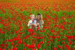 Happy family resting on a beautiful poppy field. Family having fun outdoor. Woman with child girl in field with red poppies. Mother and daughter are playing in the field of flowering red poppies.