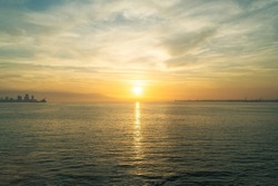 Sunset over the sea, sun in the middle of horizon, building horizon on the edges.