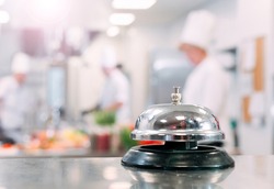 Table distribution in the restaurant. Cooks prepare food in the kitchen against the background of a metal bell