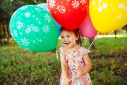 Baby girl 2-3 year old holding balloons outdoors. Birthday party. Childhood. Happiness. 