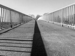Bridge over a river, with the railing as a shadow in the middle. in black and white