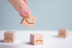 A man holds a wooden cube with a picture of a positive face on the background of negative emotions. Close up.