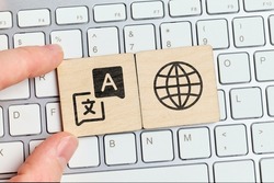 Hand holding a piece of wood with a symbol of a translator on the keyboard.