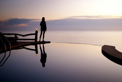 Girl silhouette by the swimming pool with sea behind at sunset