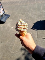 A hand holding a delicious soft ice cream with disco dip on a sunny day