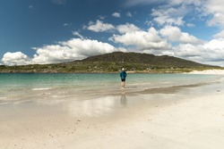 Traveler woman walking along white sand beach and clear water at Dog's Bay Galway Ireland