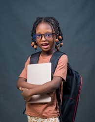 Portrait of a female African girl child or kid student from Nigeria happily looking at the camera while holding an educational smart tablet in her hands and a school back on her back