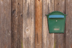 Green metal mail box hanging on right side of wooden house wall