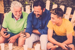 complete family caucasian people men sitting on a wodd bench looking smartphones. grandfather father and son all together enjoying the leisure outdoor time with smile and fun. technology generations