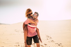 happiness concept with middle age people man carrying woman on his back walking on the soft sand of the desert dunes in totally freedom. alternative vacation and happy lifestyle