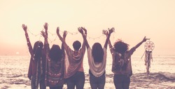 Vintage tones pictures of five women friends viewed from rear giving up hands for happiness in front ona sunset on the ocean and holding lights and a dreamcatcher for spiritual concept