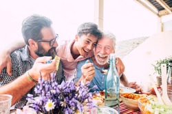 Happy people family concept laugh and have fun together with three different generations ages : grandfather father and young teenager son all together eating at lunch - outdoor home party leisure