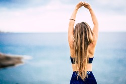 Healthy lifestyle people concept with beautiful long blonde hair girl viewed from back do some stretching in front of the ocean view outdoor - fit woman and attractive female