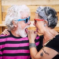 Portrait of cheerful caucasian senior crazy couple with wood background - alternative and young old people in funny expression -white hair and beard and tatoofor  diversity concept and age - youthful