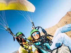 Active young adult people woman enjoy paraglide activity fliying in the sky with professional pilote in the back - cheerful happy female people fly and have fun with paragliding