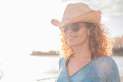 Portrait of cheerful happy middle age adult woman outdoor smiling and enjoying - young caucasian female people with hat and sunglasses - ocean beach in defocused background