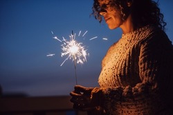 Adult woman with closed eyes holding sparkler in the night with blue sky in background - new year eve christmas holidays - female people with firework outdoor enjoy emotions and feeling