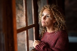Thoughtful portrait of attractive adult woman at home looking outside the windows reflected on the gass. Worried adult female people alone indoor. Depression sadness concept