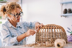 Creative handwork at home in indoor hobby leisure activity for female people realizing wicker lamp or basket on the table. Happy woman working at home for interior furniture making of