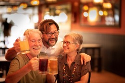Happy family mixed generations adult and old senior people enjoy celebrating together clinking beers in a restaurant pub and looking for a nice picture