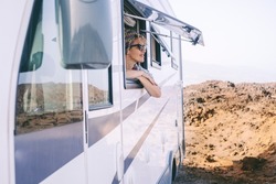 Summer holiday travel vacation with renting camper van motor home. Happy woman admiring outside the window the nature. Scenic destination vanlife lifestyle. Tourist enjoying arrival at the beach