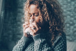 Side view of woman blowing nose for flu influenza symptoms in winter at home. Temperature reduction indoor to save energy gas costs. Female people with virus contagion using paper tissues. Disease