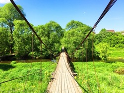 panorama landscape, forest river among green fields above it a wooden suspension bridge, on a summer day with stunning white clouds and blue sky, day or dawn in a spring field with green grass, path