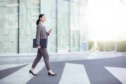 Asian woman with smartphone walking against street blurred building background, Fashion business photo of beautiful girl in casual suite with smart phone. 
