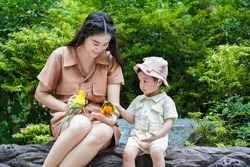 Asian young woman feeding birds on hand and showing to her daughter in the zoo.