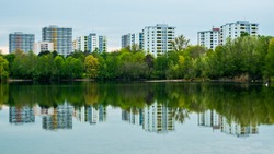 
Green symmetry at lake, green trees and city buildings symmetrical reflected in lake